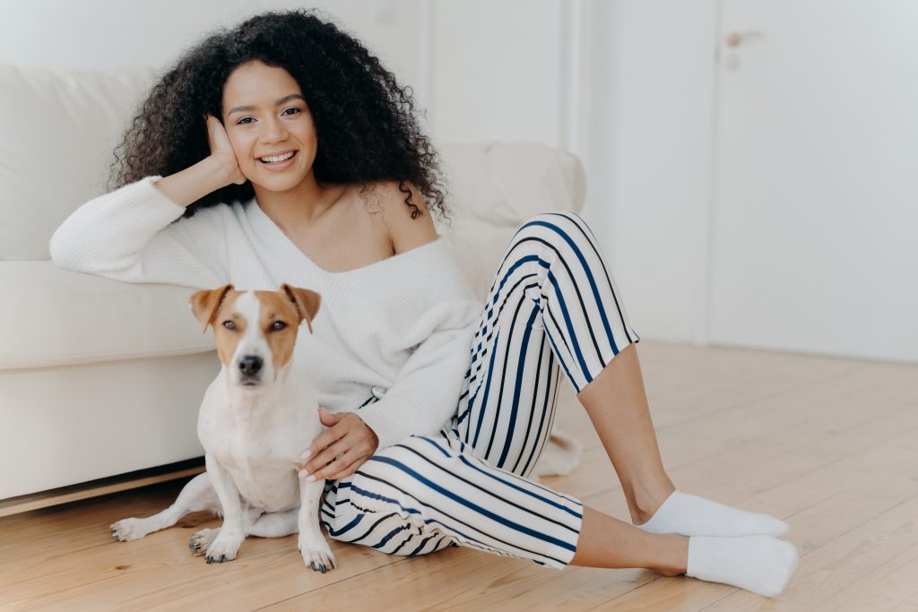 Woman sitting on floor with a dog, leaning against a sofa.
